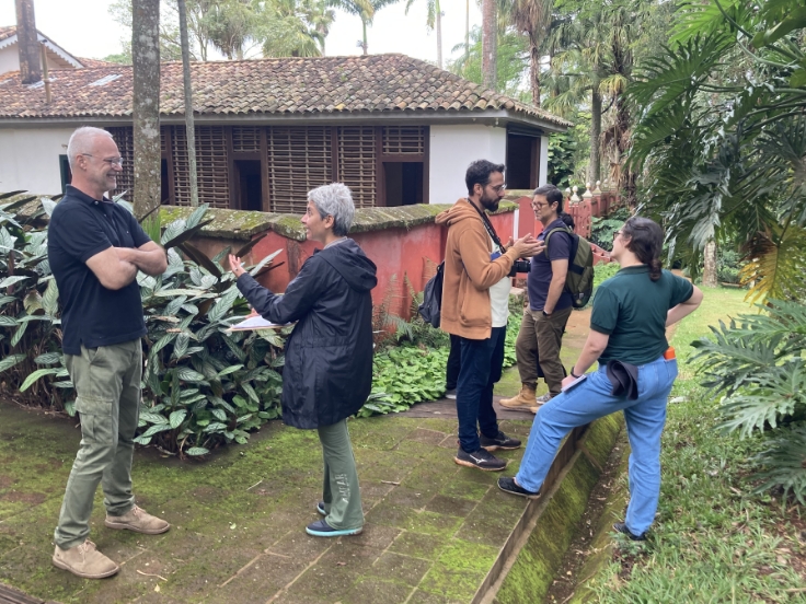 Foto de pessoas de pé, em área externa ajardinada. À esquerda, um homem e uma mulher conversam. À direita, um homem conversa com uma mulher e, atrás deles, outro homem acompanhado de mais duas pessoas que não aparecem por inteiro na foto. Sabemos que se trata de profissionais trabalhando na implantação do Plano Diretor de Gestão Patrimonial da Fazenda do Pinhal.